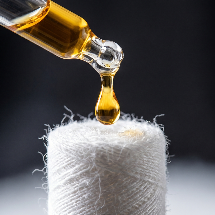 A glass dropper applying a golden liquid drop to a white cotton wick to demonstrate the coil priming process