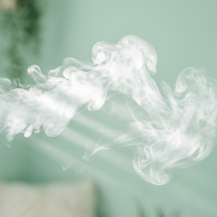Abstract white vapor cloud drifting horizontally across a blurred mint green room interior with soft lighting